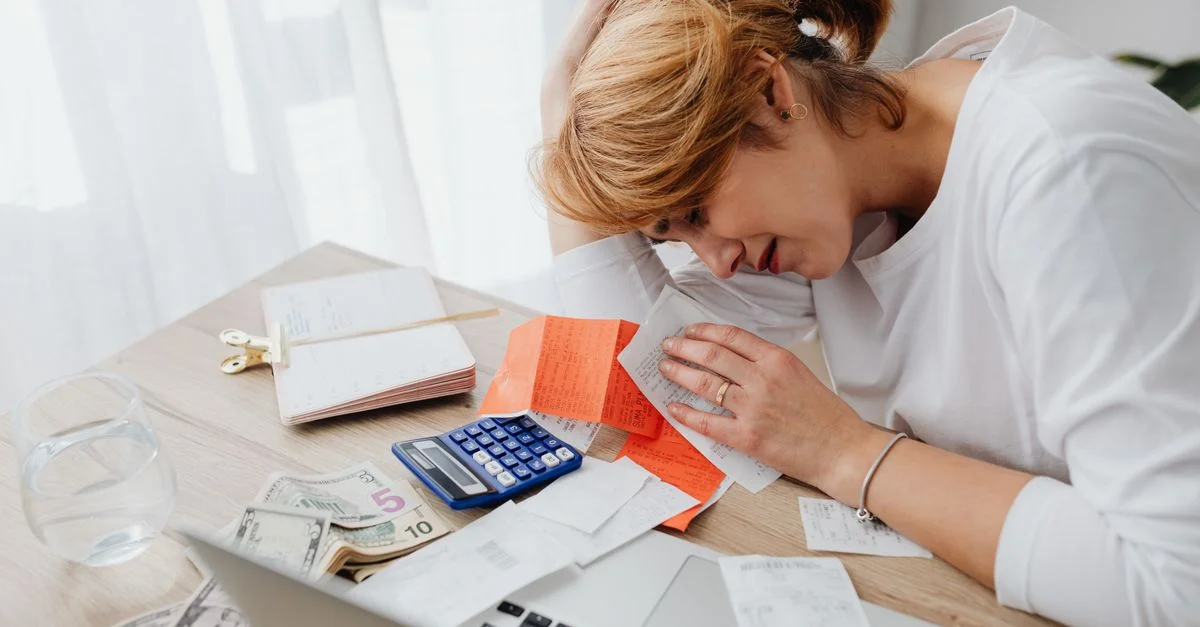 Une femme débordée par ses finances, entourée de factures, d'une calculatrice et d'espèces chez elle.