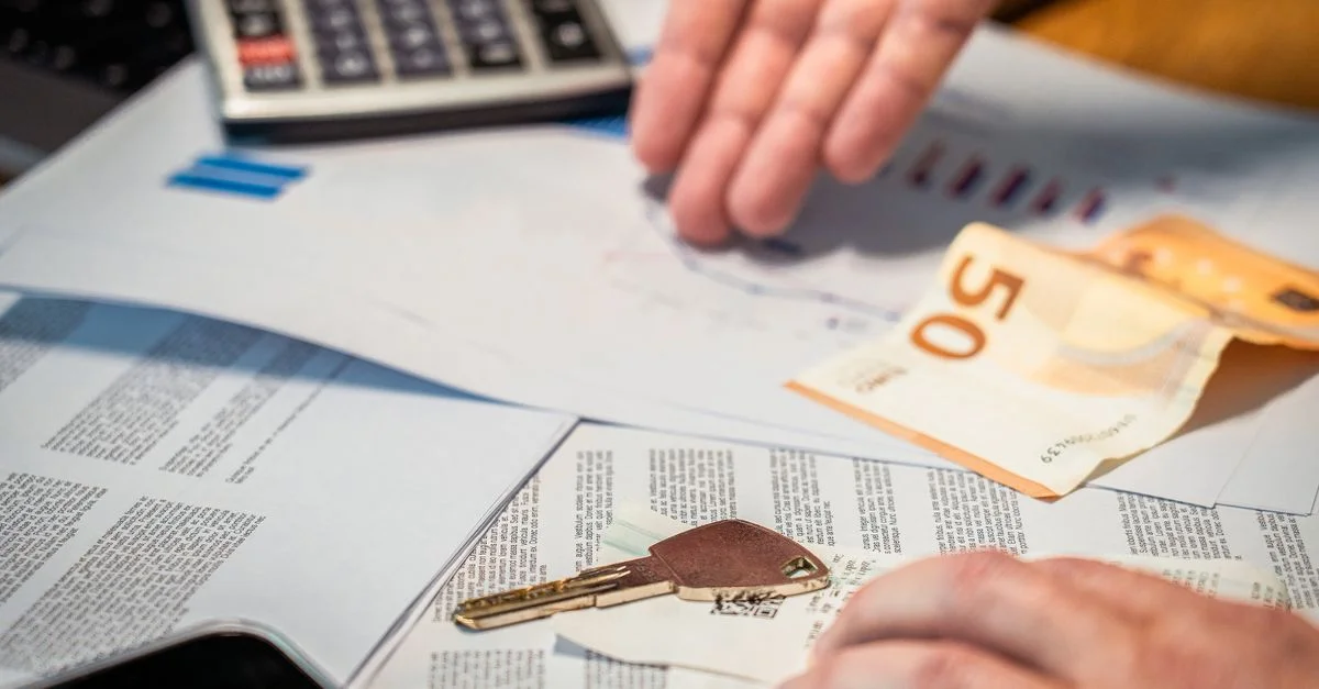 Mains examinant des documents financiers, un billet de 50 euros et une clé, suggérant des thèmes d'investissement ou d'immobilier.
