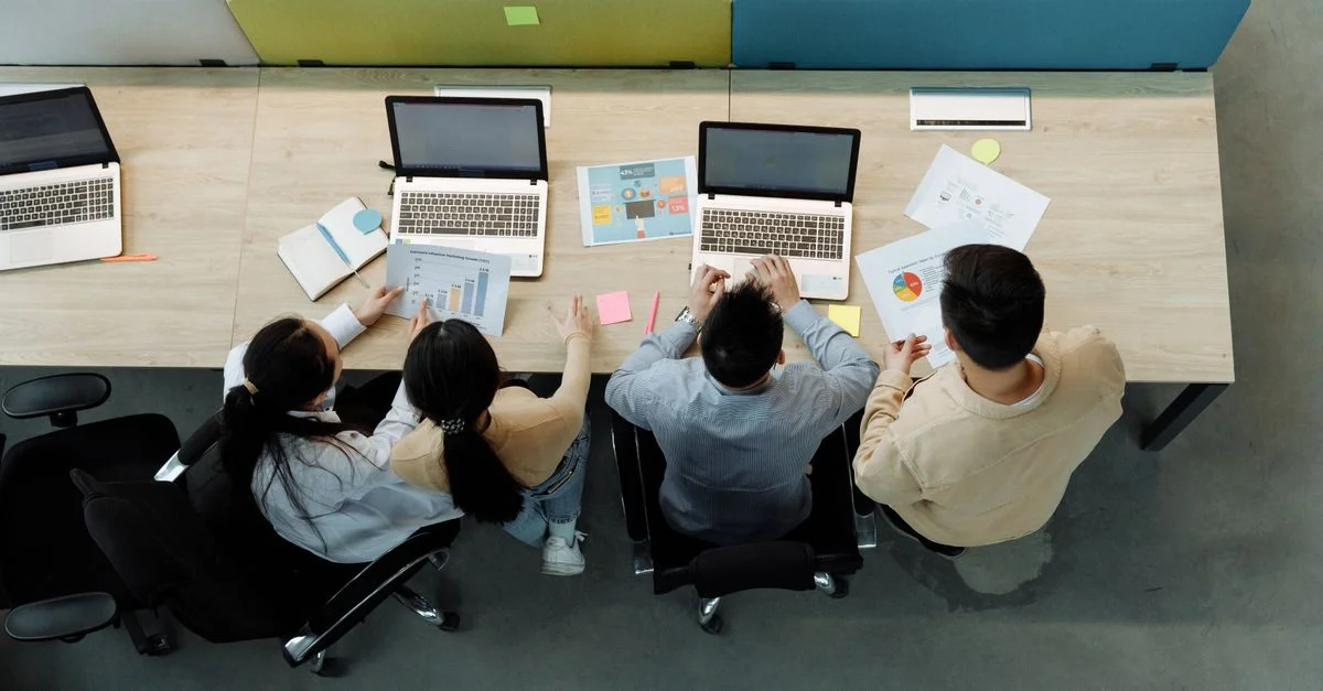 Vue aérienne de quatre collègues travaillant avec des ordinateurs portables et des documents à un bureau partagé.