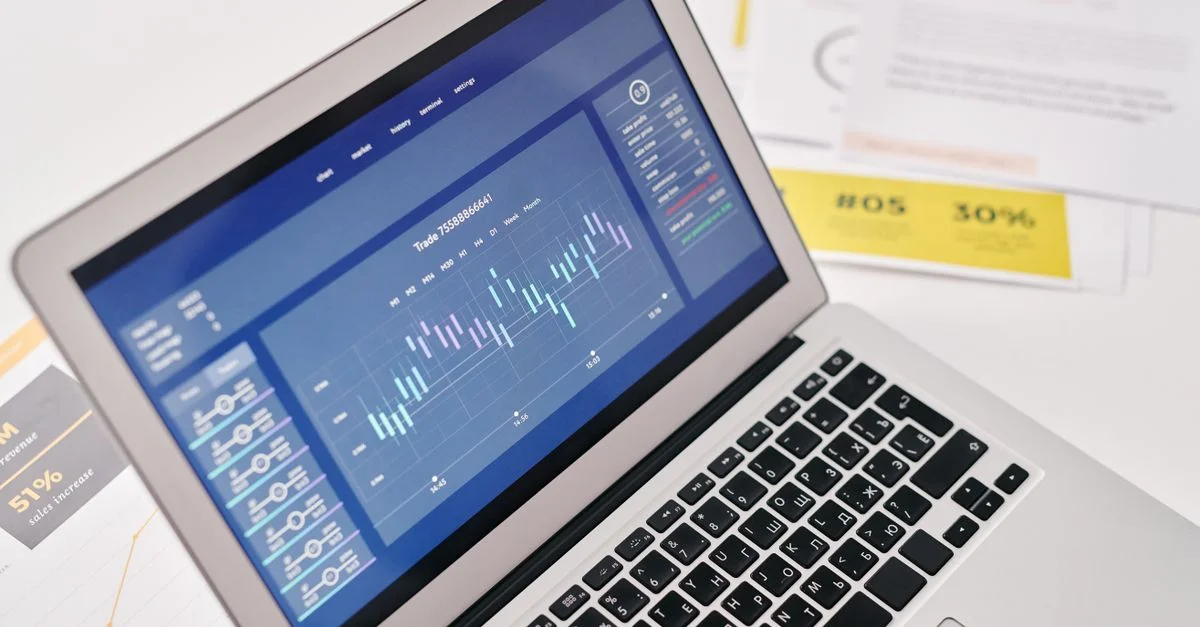 Ordinateur portable ouvert affichant des graphiques financiers et des analyses avec des documents à proximité, idéal pour des présentations commerciales.