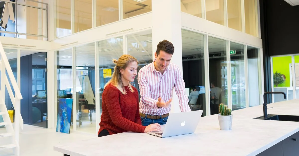 Deux collègues collaborant dans un bureau moderne avec un ordinateur portable.