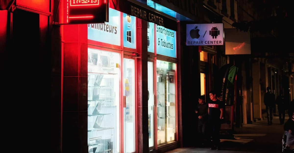 Scène nocturne vibrante d'un magasin de réparation de smartphones éclairé avec une enseigne rouge.